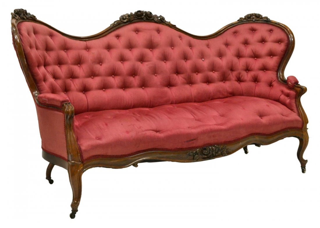 AMERICAN VICTORIAN FLORAL CARVED UPHOLSTERED SOFA: American Victorian carved and upholstered sofa, 19th c., Rococo floral carved shaped walnut frame descending to padded arms with scrolled hand holds, tufted and buttoned pink fabric upholstered seat a