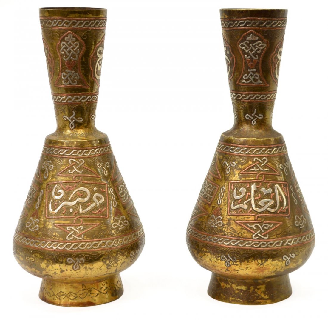 (2) ISLAMIC MAMLUK CAIROWARE MIXED METAL VASES: (pair) Islamic Mamluk Cairoware mixed metal vases, each having a long neck over a tapered body, rising on circular foot, brass base with copper and silver foliated arabesque motifs, reserved Arabic sc