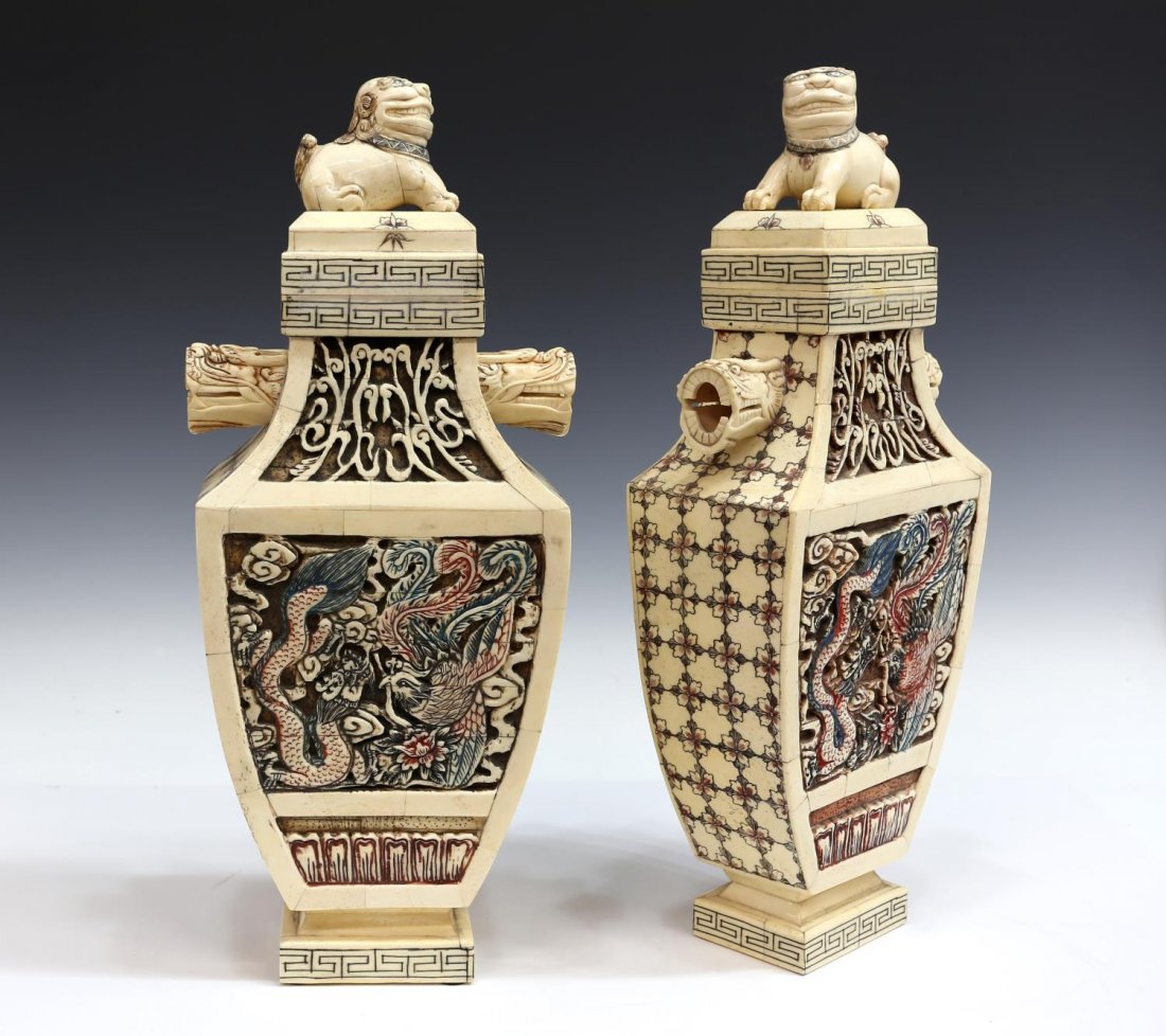(PAIR) CHINESE CARVED BONE LIDDLED SQUARE VASES: (pair) Chinese carved & tiled bone squared urn-form vases, each surmounted with a fu-dog lid, over the tapered neck, with open-mouthed dragon handles, the body decorated with recessed dragon and phoen