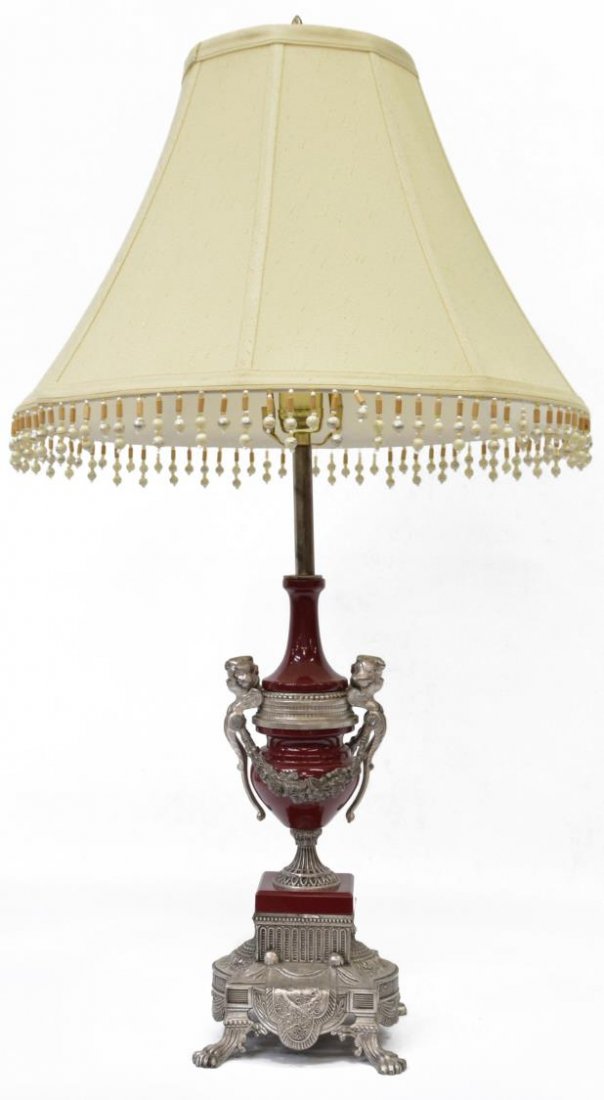 LOUIS XVI STYLE PORCELAIN & METAL PUTTI TABLE LAMP: Louis XVI style silvered metal and porcelain table lamp, Italy, having a single light over the red porcelain urn form standard, decorated with putti masks and floral swag, circular foot, rising on sha