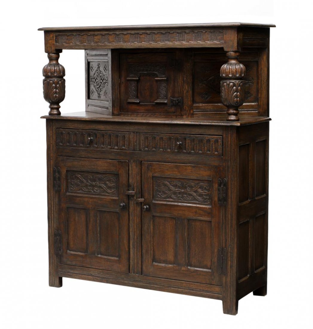 ENGLISH OAK COURT CUPBOARD: English oak court cupboard, 20th c., a stepped cornice with bulbous supports flanking the central door and angled sides, below are two lower frieze drawers and two doors, rising on block feet, 57.5"h,