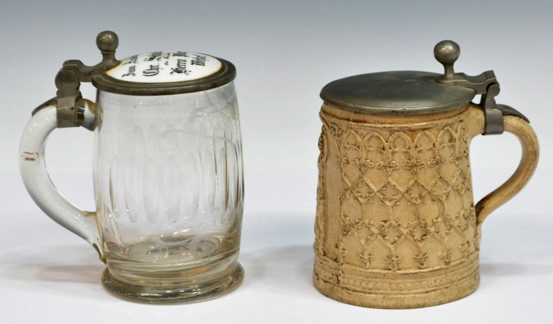 (2)ANTIQUE GERMAN GLASS & GOTHIC STYLE BEER STEINS: (lot of 2) Antique beer steins: (1) stoneware stein, having hallmarked pewter lid, the body with raised Gothic tracery and reserved figure, 6"h; (1) German stein, etched and cut colorless body, surmou
