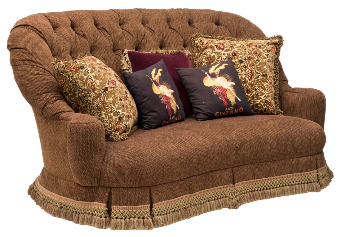 LARGE BUTTONED FABRIC SOFA: Large arched back settee upholstered in buttoned rust fabric with tiny red and white accents including the tasseled skirt, rising on squared tapered legs, together with (5) multi color throw pillows o