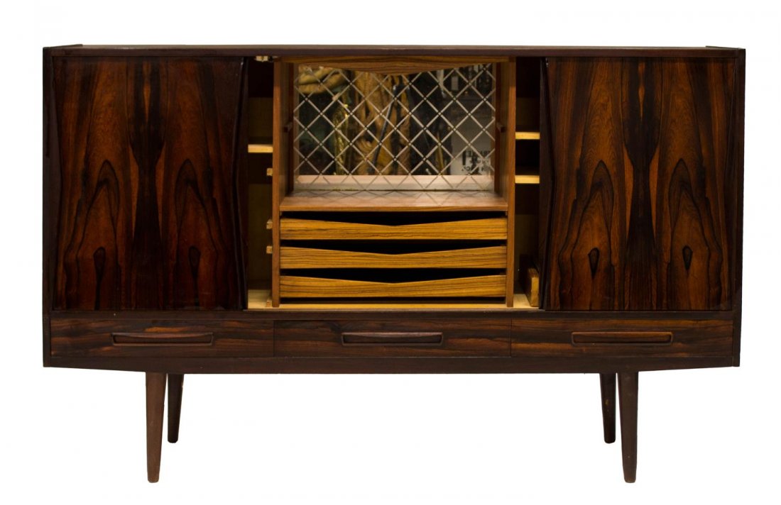 DANISH MID-CENTURY MODERN ROSEWOOD SIDEBOARD: Danish mid-century modern rosewood sideboard, c. 1950's, the rectangular case fitted with four sliding doors concealing adjustable shelving and rolling drawers, mirrored back wet bar to center above s