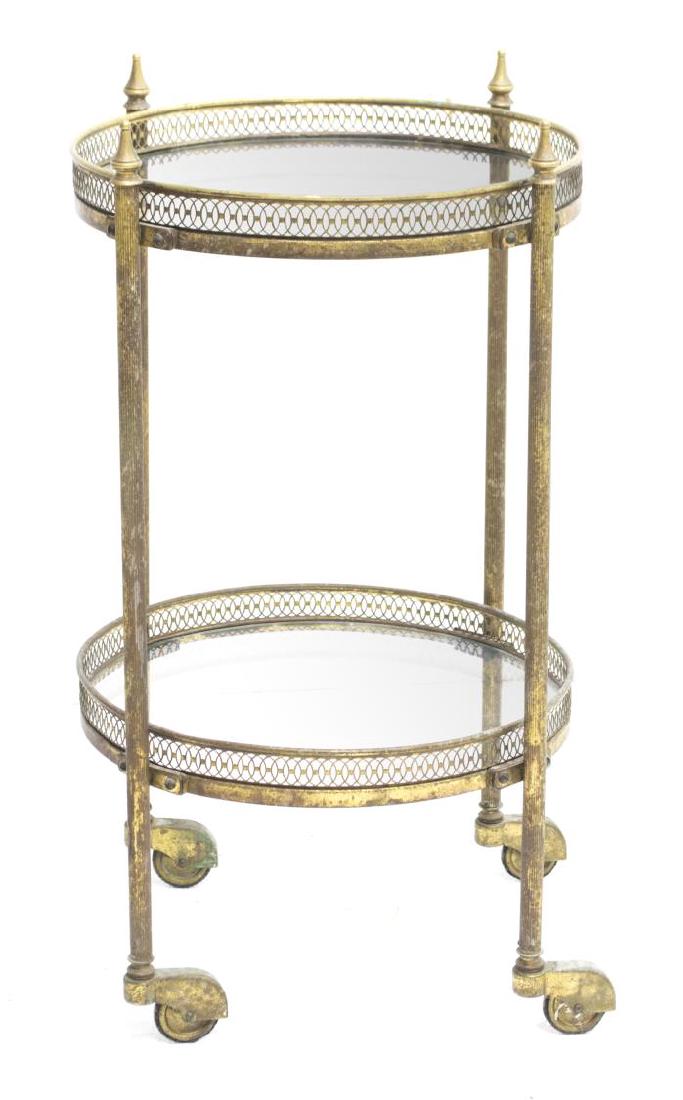 ROUND GLASS TOP & BRASS SERVICE CART: Continental glass and brass service cart, round glass top sitting in fitted metal frame, with pierced metal border, over medial shelf, on casters, patination and surface wear, 25"h, 16.5"diam Start Pr