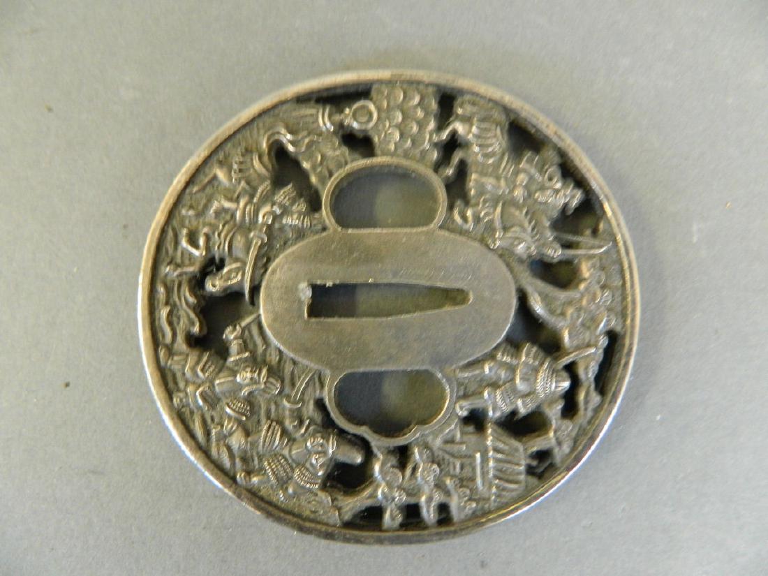 A Japanese white metal tsuba with pierced and engraved: A Japanese white metal tsuba with pierced and engraved decoration of samurai