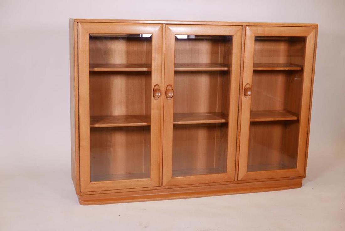 An Ercol blonde ash three door bookcase with bevelled: An Ercol blonde ash three door bookcase with bevelled glass, 54" x 11" x 38"