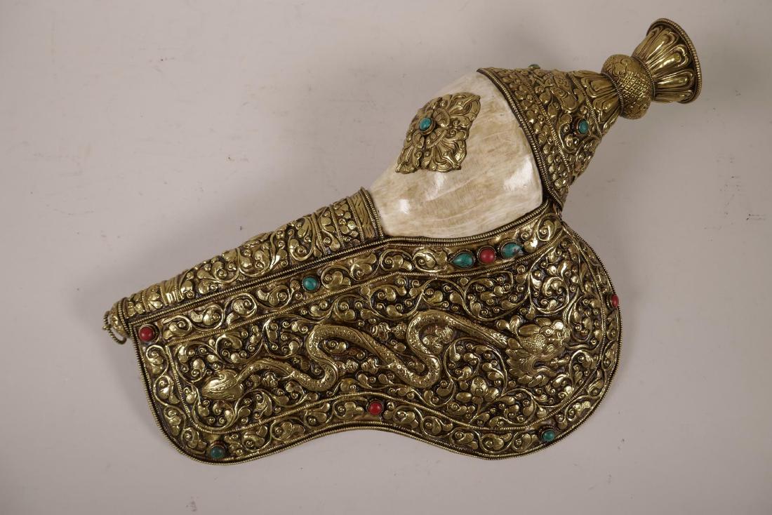A large Tibetan brass mounted conch shell with repoussé: A large Tibetan brass mounted conch shell with repoussé dragon and vajra decoration, set with semi-precious decorative stones, 16" x 10½"