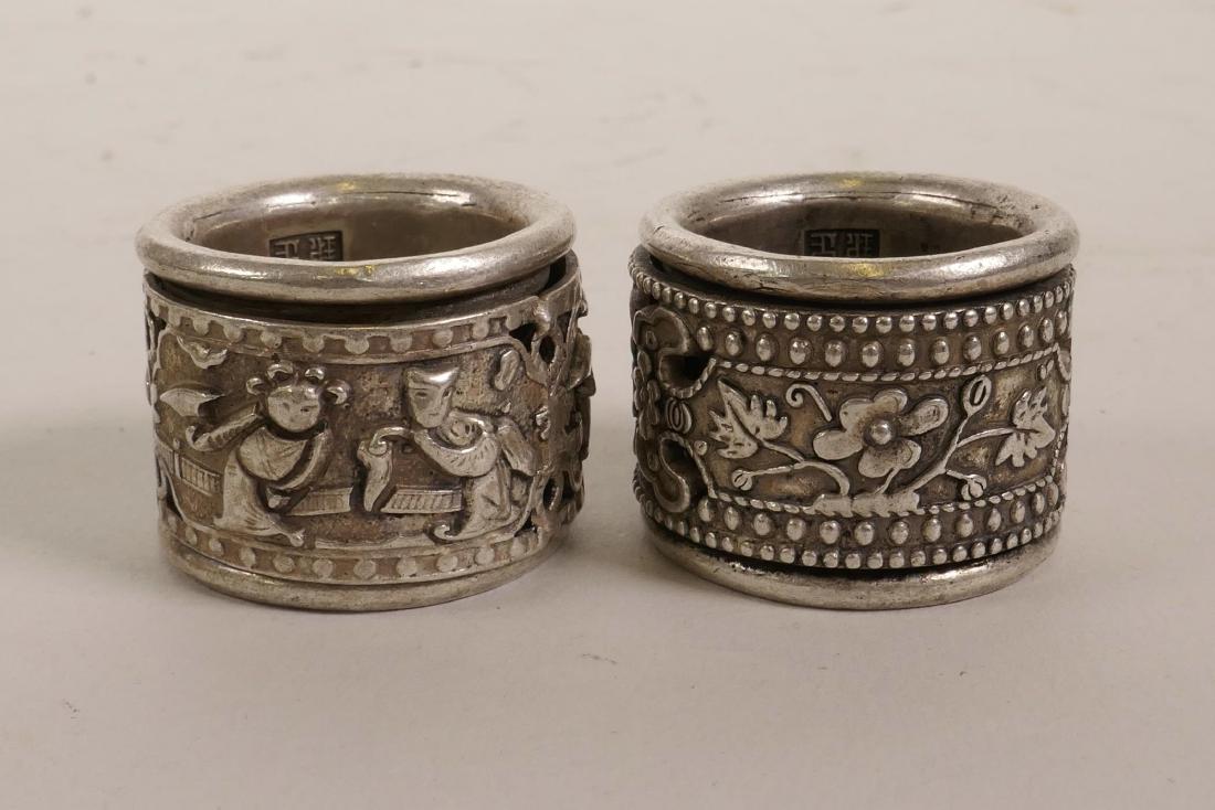 A Chinese white metal archer's thumb ring with a: A Chinese white metal archer's thumb ring with a revolving cuff decorated with flowers, and another similar