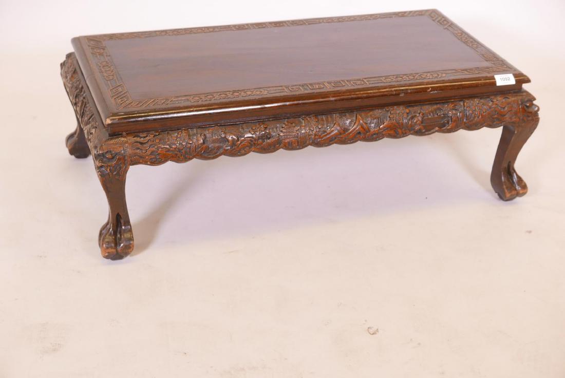 A Chinese teak low table, with carved frieze and top,: A Chinese teak low table, with carved frieze and top, raised on cabriole supports with paw feet, 33" x 18" x 11"