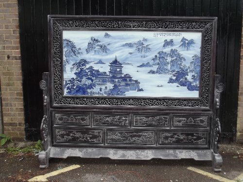 A superb Chinese hardwood framed blue and white pottery: A superb Chinese hardwood framed blue and white pottery screen, painted with pavilions by a lake and mountain landscape, the frame carved with figures and landscapes,signed, 90½'' x 74''