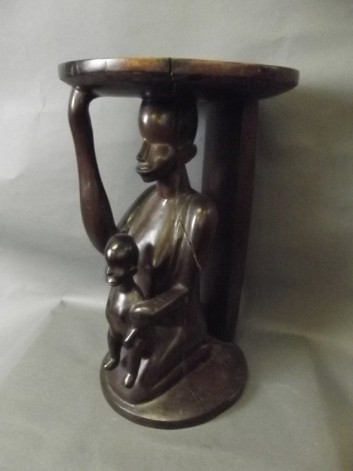 An African carved hardwood stool depicting a kneeling: An African carved hardwood stool depicting a kneeling mother with a child on her lap, 21'' high