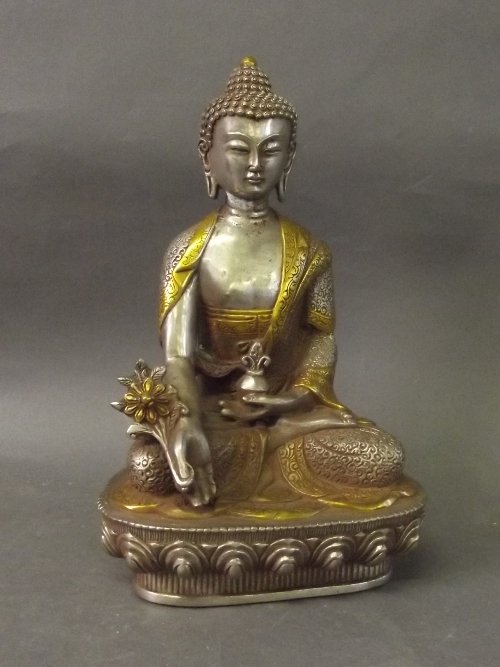 A Tibetan seated white metal and gilt wash embellished: A Tibetan seated white metal and gilt wash embellished figure of Buddha holding flowers, sitting on a stylised lotus throne, 8'' high