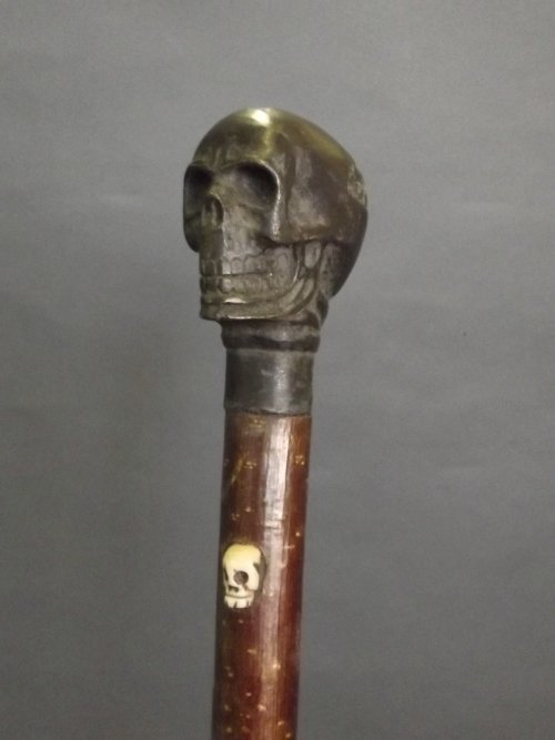 A walking stick with bronze handle in the form of a: A walking stick with bronze handle in the form of a skull, and a smaller bone skull inlaid into the stick, 36¼'' long