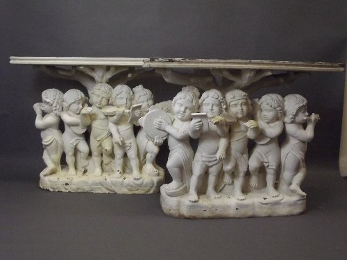 A pair of gessoed carved wood painted console tables su: A pair of gessoed carved wood painted console tables supported by cherub musicians, 42'' wide, 35'' high