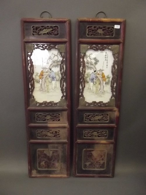 A pair of Chinese porcelain panels depicting a: A pair of Chinese porcelain panels depicting a fisherman and companion beneath a tree, mounted in an ornate carved hardwood frame, 51'' x 14''
