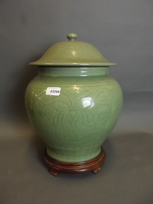 A large C19th Chinese celadon glazed jar and cover with: A large C19th Chinese celadon glazed jar and cover with incised decoration, on a wooden stand, 18'' high