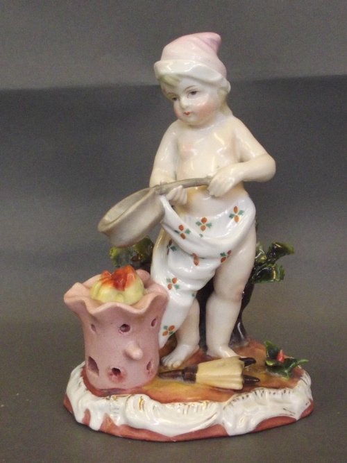 A Continental figure of a young boy standing by a fire: A Continental figure of a young boy standing by a fire with a saucepan and a pair of bellows at his feet, crossed swords mark, 6'' high