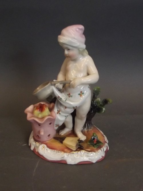 A Continental figure of a young boy standing by a fire: A Continental figure of a young boy standing by a fire with a saucepan and a pair of bellows at his feet, crossed swords mark, 6'' high