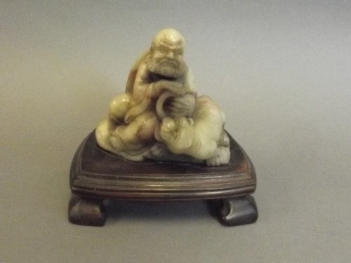 A Chinese carved soapstone figure of a seated deity: A Chinese carved soapstone figure of a seated deity with kylin, on a wood stand, 4'' high
