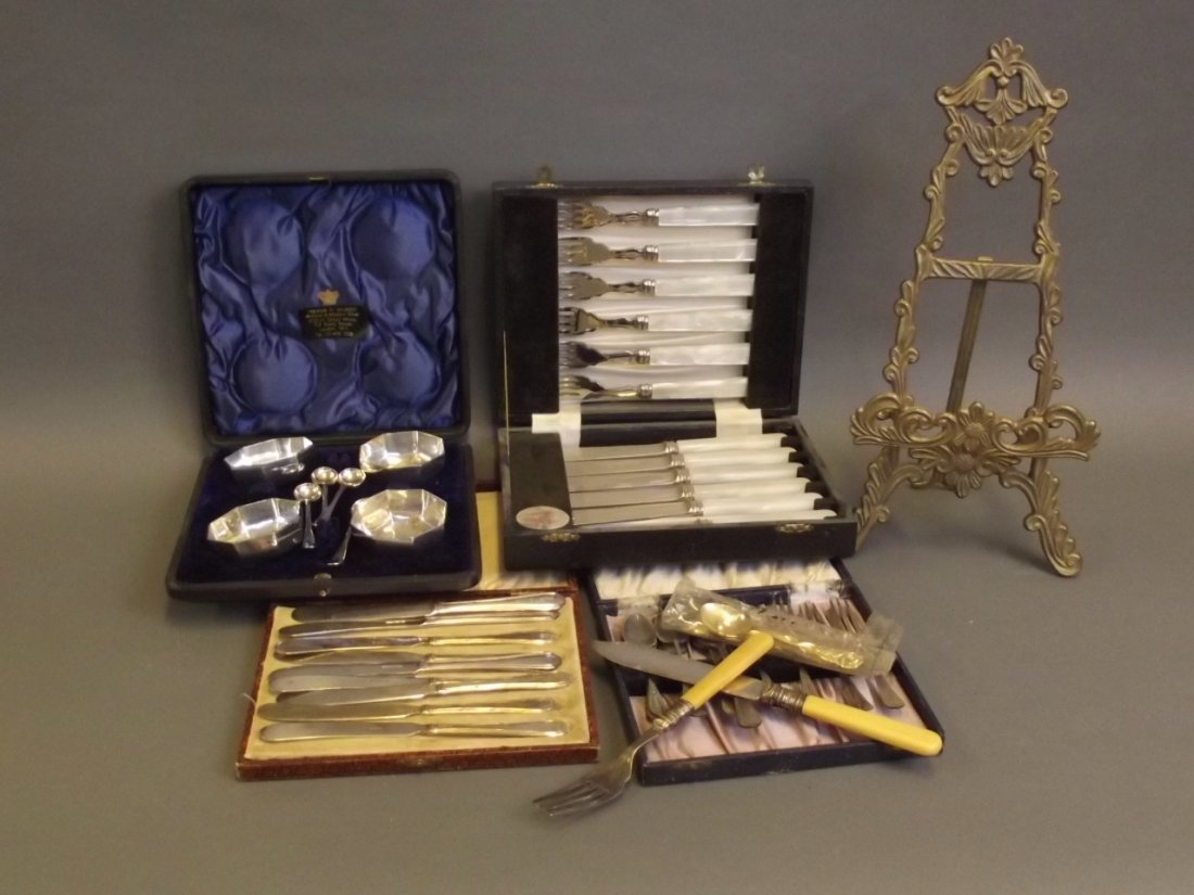A boxed set of plated butter knives, cake forks and: A boxed set of plated butter knives, cake forks and spoons, a boxed set of table salts and spoons, dessert knives and forks, and gilt metal easel frame, 14'' high