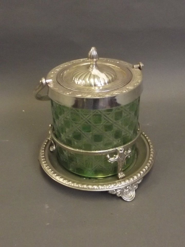 A circular silver plate and green cut glass biscuit: A circular silver plate and green cut glass biscuit barrel with ornate engraved floral decoration, 7¼'' x 7½''