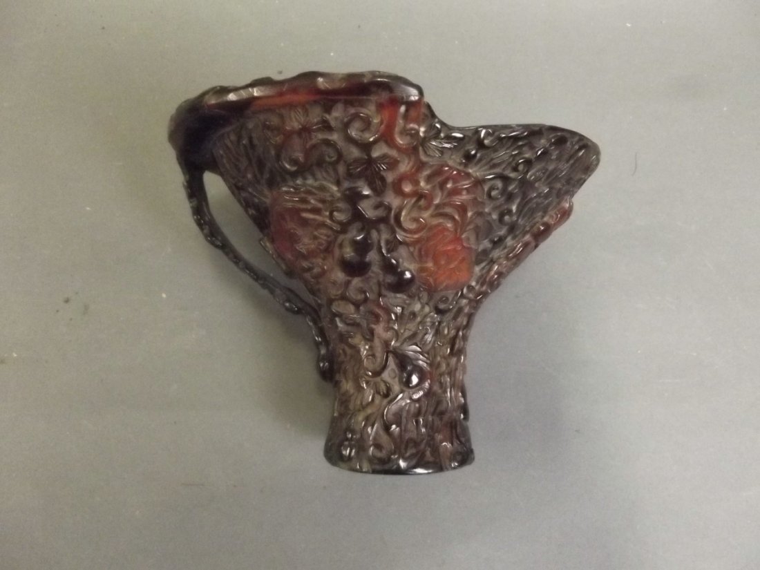 A large Chinese carved horn libation cup decorated with: A large Chinese carved horn libation cup decorated with figures in a stylised forest, 5'' high