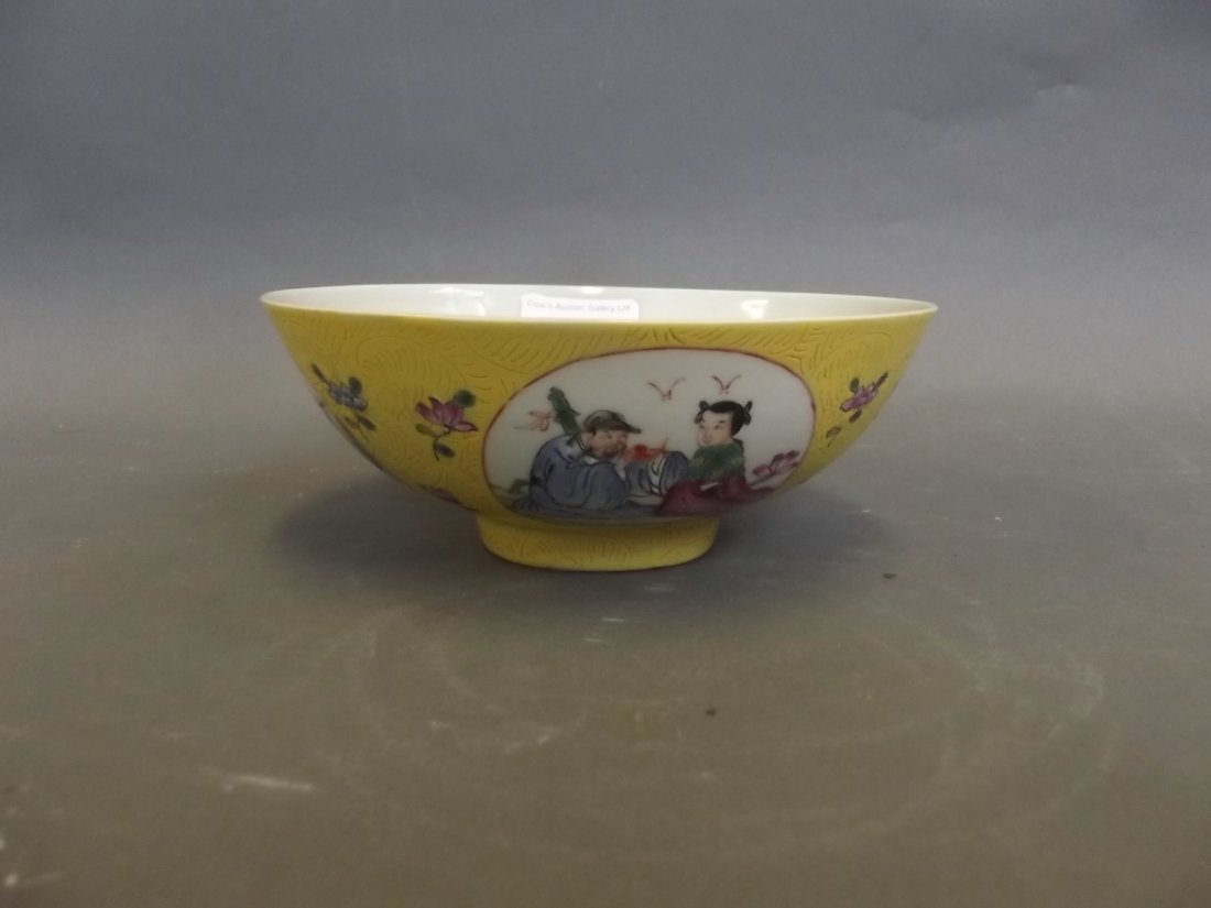 A yellow ground Chinese bowl with decorative panels: A yellow ground Chinese bowl with decorative panels depicting figures seated in a garden, marked, 6¼'' diameter