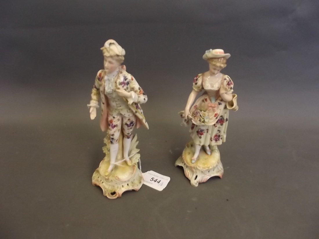 A pair of Continental porcelain figures of a man and: A pair of Continental porcelain figures of a man and woman standing on rococo bases wearing floral painted clothing and feathered hats, 8¼'' high (AF)