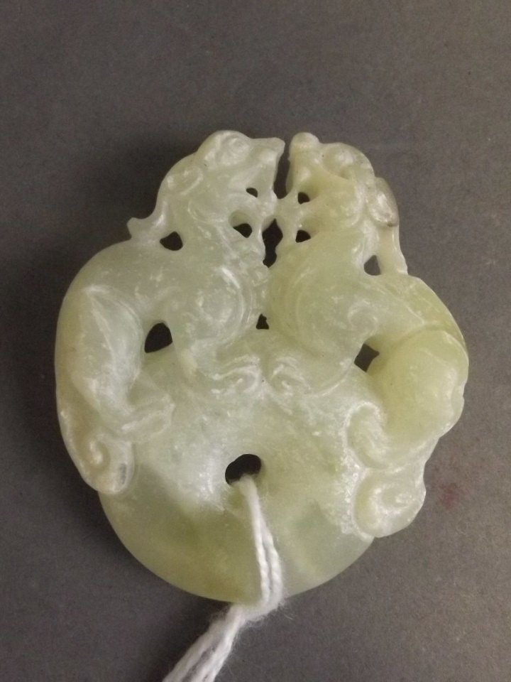 A Chinese cream jade pendant with carved decoration of: A Chinese cream jade pendant with carved decoration of dragons standing atop a pi-disc, 1¾'' high
