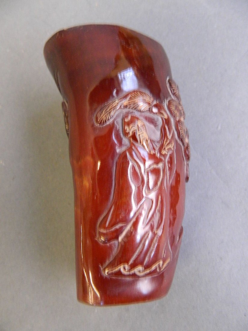 A Chinese horn libation cup carved with a sage standing: A Chinese horn libation cup carved with a sage standing by a tree, 4'' long