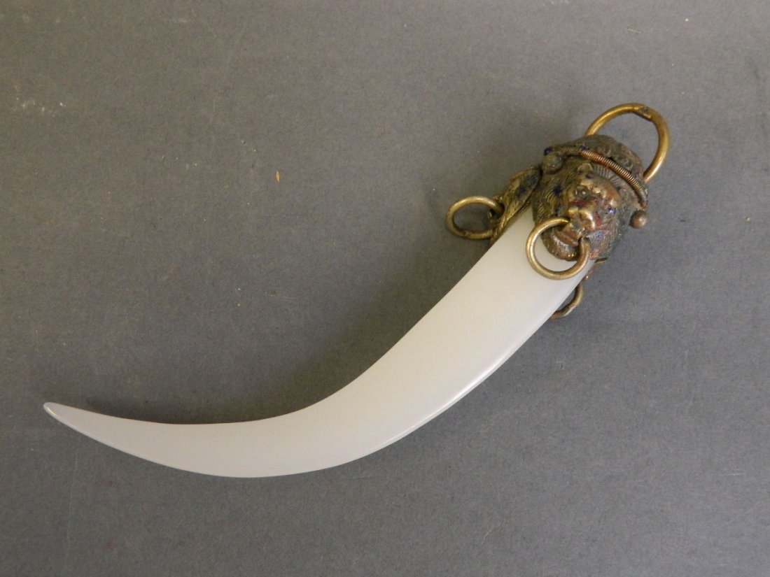 A celadon jade pendant in the form of a claw, with a: A celadon jade pendant in the form of a claw, with a metal mounted end depicting ringed lion heads, 6'' long