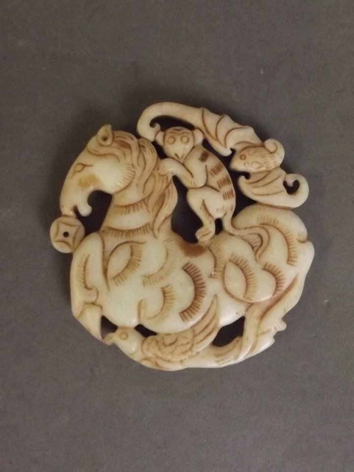 A Chinese white jade circular pierced pendant with: A Chinese white jade circular pierced pendant with carved decoration of a bat and monkey riding a horse, 2¾'' diameter