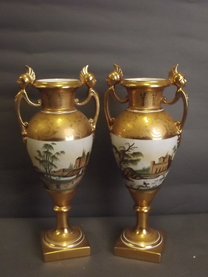 A pair of twin handled porcelain vases decorated with: A pair of twin handled porcelain vases decorated with Continental landscape scenes on a matt and bright gilt ground, 16½'' high