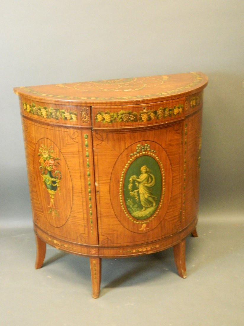 A late C19th/early C20th satinwood demi-lune side: A late C19th/early C20th satinwood demi-lune side cabinet with painted decoration after Angelica Kaufmann, on four sabre supports, 36'' high