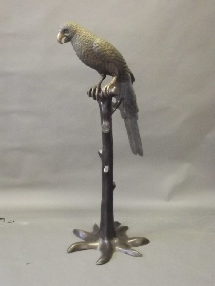 A large bronze figure of a parrot perched on a tree: A large bronze figure of a parrot perched on a tree stump, 48'' long