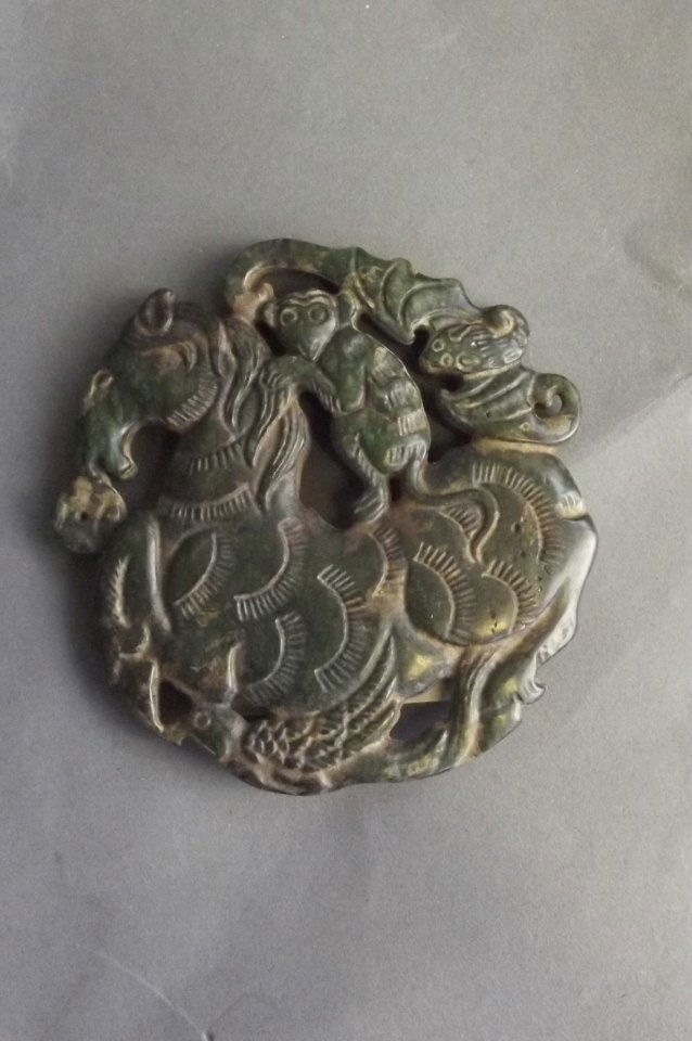 A Chinese pierced and carved hardstone pendant: A Chinese pierced and carved hardstone pendant decoration with a monkey riding a horse and a bat in flight, 2¾'' diameter
