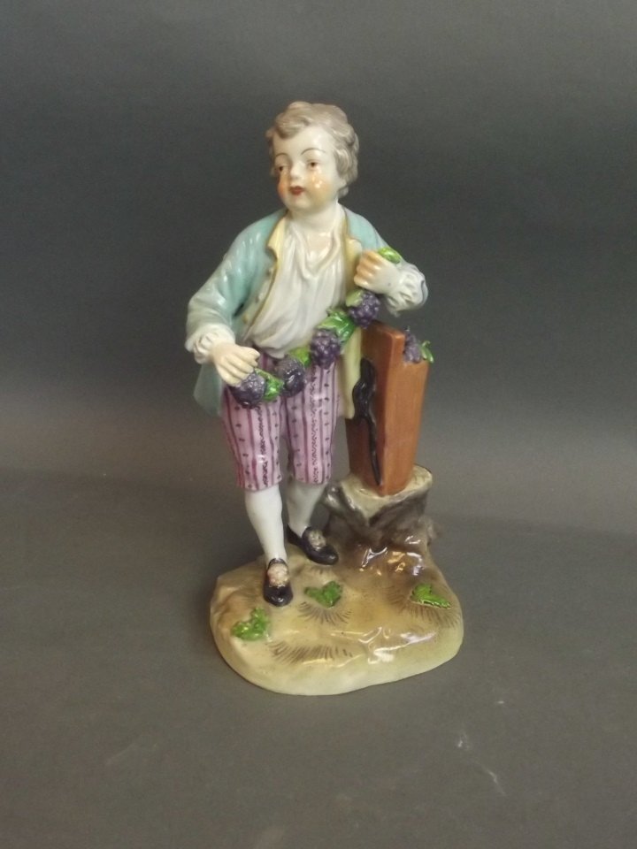 A C19th/C20th Dresden figure of a boy holding a garland: A C19th/C20th Dresden figure of a boy holding a garland of grapes, 6½'' high