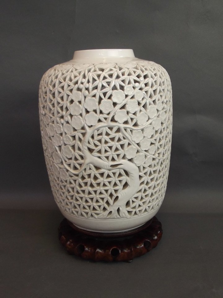 A reticulated Chinese blanc-de-chine vase decorated: A reticulated Chinese blanc-de-chine vase decorated with a flowering tree, on a carved wood stand, drilled, 13½'' high