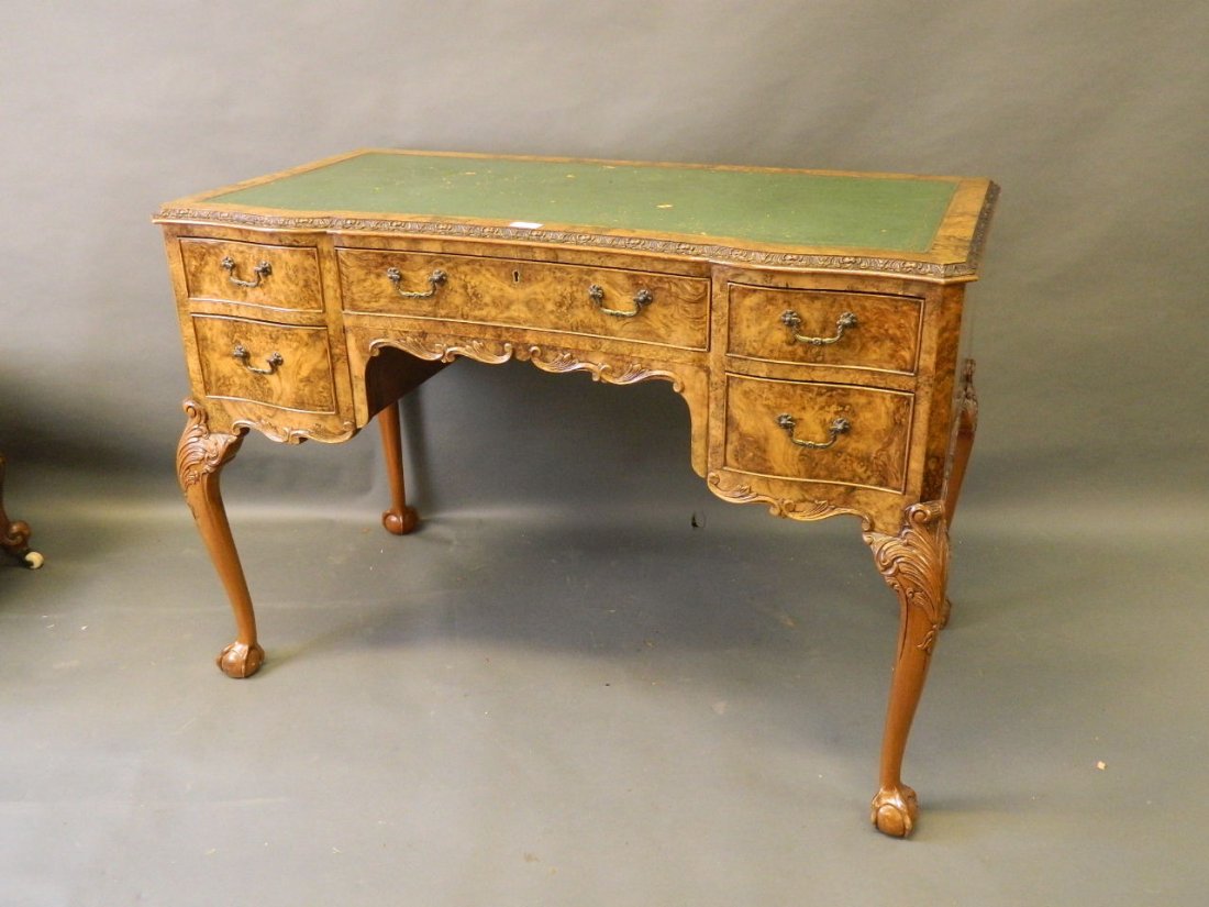 A burr walnut shaped front five drawer kneehole desk: A burr walnut shaped front five drawer kneehole desk with inset leather top, standing on carved cabriole legs and ball and claw feet, back veneered, 23'' x 43'' x 30''