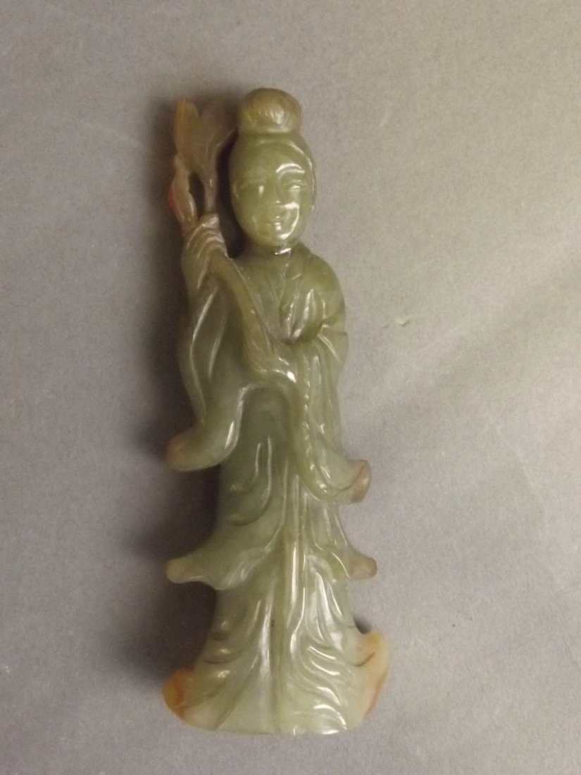 A Chinese olive green jade pendant carved in the form: A Chinese olive green jade pendant carved in the form of Quan Yin holding a ruyi, 3'' high