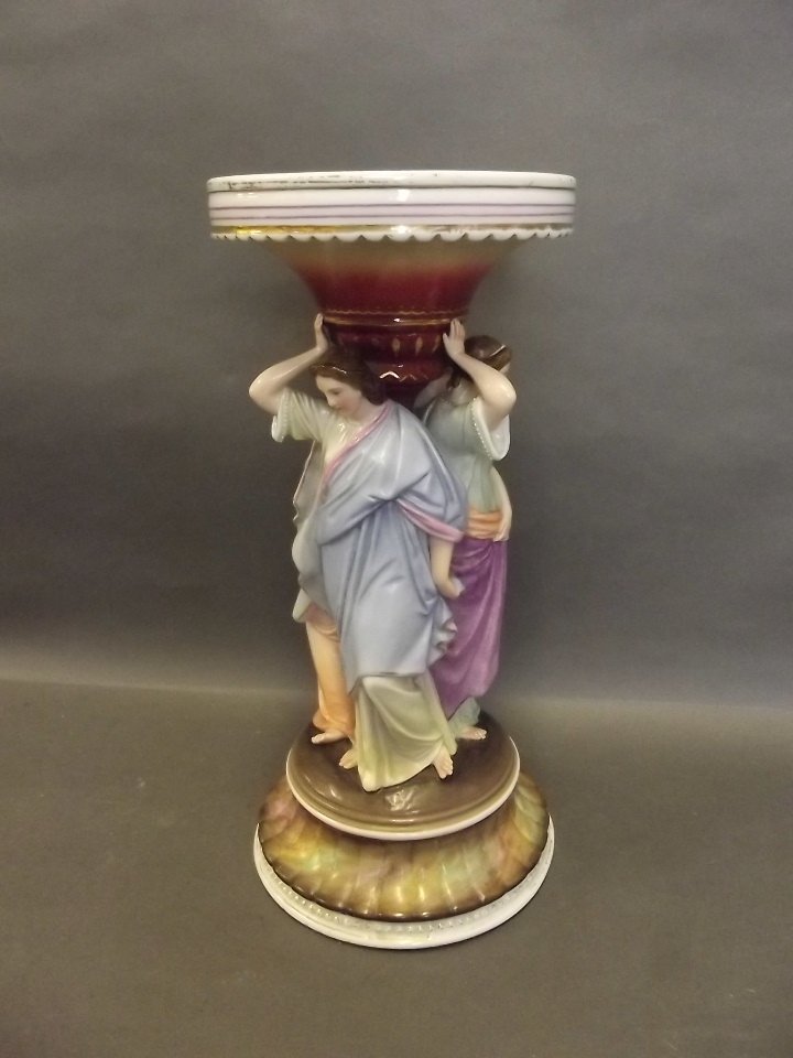 A Continental ceramic centrepiece formed as three: A Continental ceramic centrepiece formed as three classical ladies standing under a pillar, 12'' high