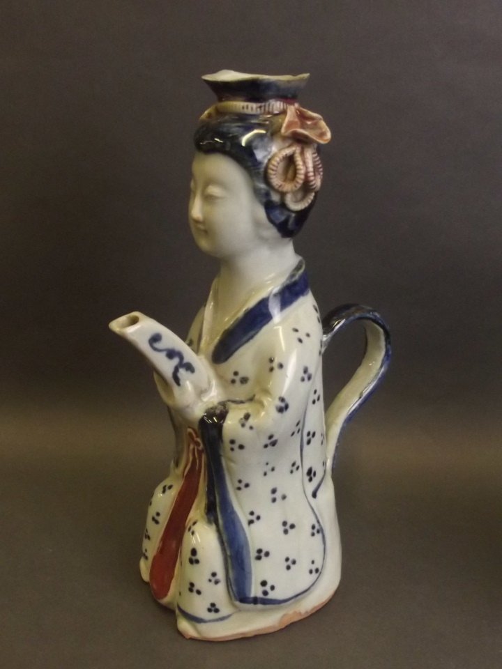 A Chinese earthenware wine jug in the form of a woman: A Chinese earthenware wine jug in the form of a woman holding the spout, 9'' high