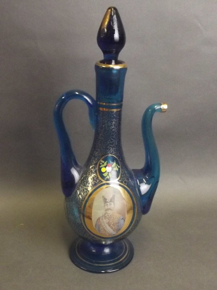 A late C19th Bohemian Persian market blue glass ewer: A late C19th Bohemian Persian market blue glass ewer and stopper, with gilt decoration and an applied print portrait of Muzaffar al-Din, Shah of the Qajar Dynasty, 10½'' high (spout AF)
