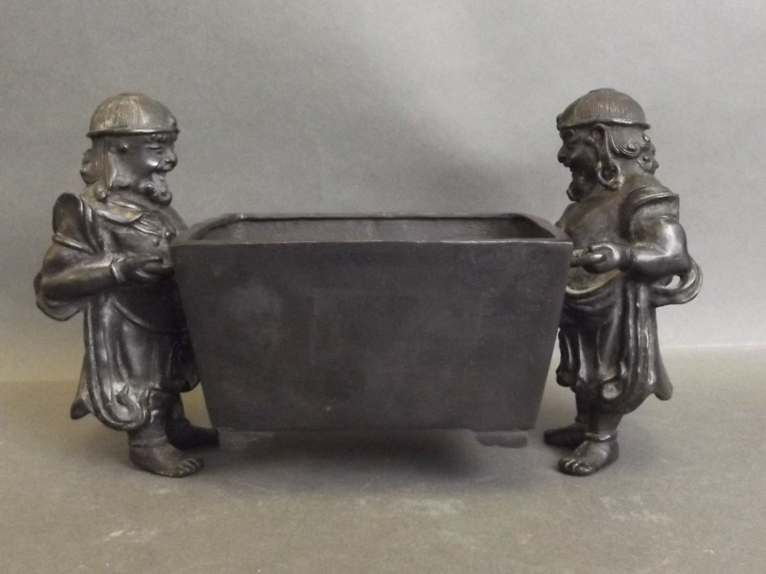 A Chinese bronze censer in the form of two men holding: A Chinese bronze censer in the form of two men holding a large trough, impressed mark to base, 8'' wide