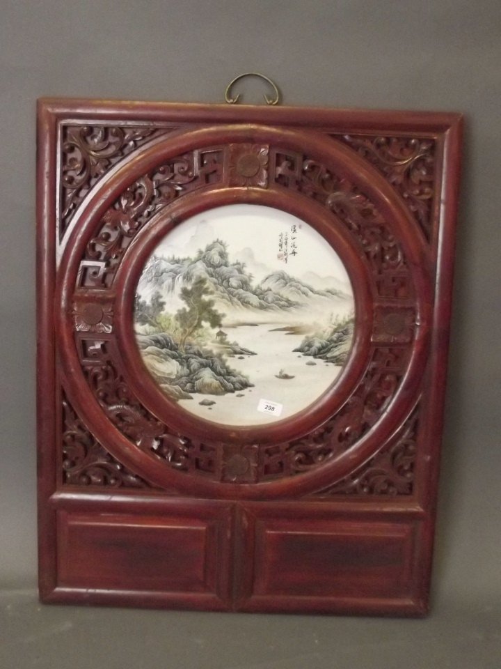 A Chinese circular porcelain panel with enamelled: A Chinese circular porcelain panel with enamelled lakeside landscape decoration, mounted in a well carved and pierced hardwood frame, 25'' x 32''