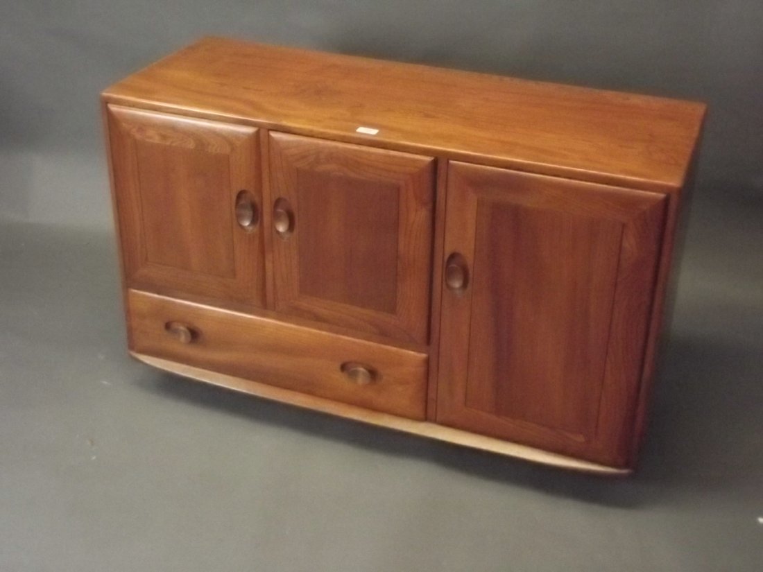 An Ercol elm sideboard, the side cupboard with fitted: An Ercol elm sideboard, the side cupboard with fitted removable tray, raised on castors, 45'' x 17'', 28'' high