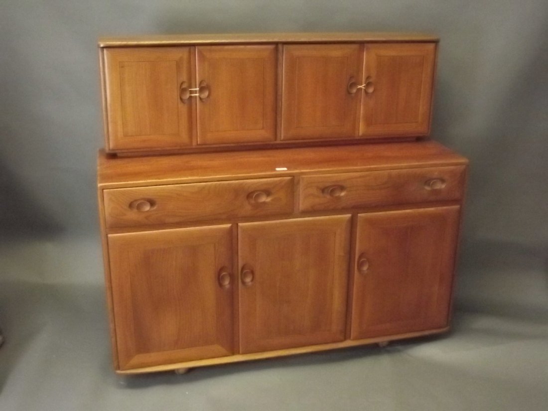 An Ercol elm sideboard with two drawers over three: An Ercol elm sideboard with two drawers over three cupboards, with canteen slide, the upper section of two cupboards, raised on castors, 54'' x 18'', 48'' high