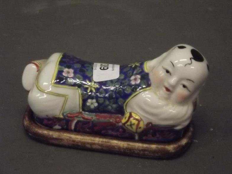A Chinese porcelain figure of a recumbent boy, on a: A Chinese porcelain figure of a recumbent boy, on a wood stand, 6" long