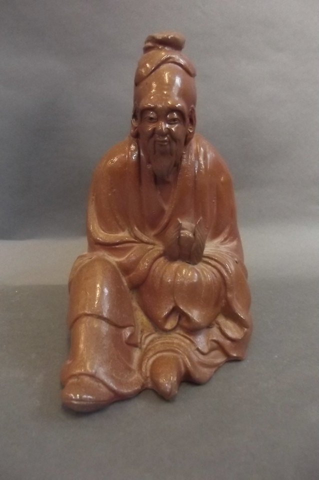 An Oriental glazed terracotta figure of a sage holding: An Oriental glazed terracotta figure of a sage holding a peach whilst seated, 9" high